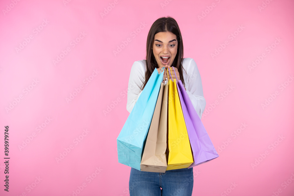 Pink background. Happy girl hold shopping bag. Cute girl holding piles of shopping bags on both hands isolated over pink background. Shopping, sales, black friday concept.