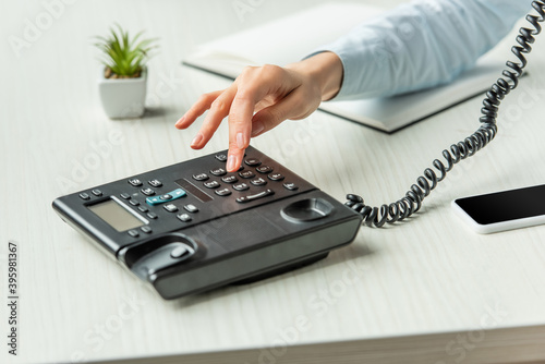 Quadro su tela Cropped of businesswoman dialing number on landline telephone on table with note