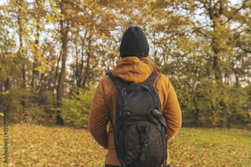 Woman in a yellow jacket with her hends in her pockets and a backpack on her back walking trough the woods in the fall © Small365