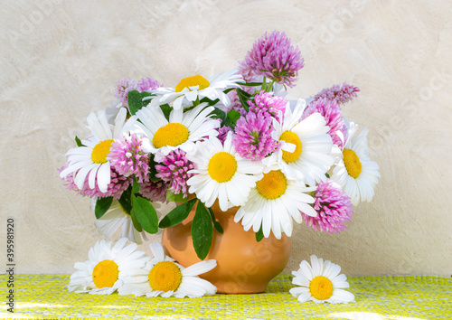 Clover and chamomile bouquet in a vase on a light background . Summer bouquet of garden and field flowers. Still life with daisies. selective focus