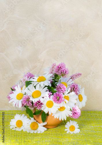 Clover and chamomile bouquet in a vase on a light background . Summer bouquet of garden and field flowers. Still life with daisies.