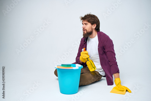A man lies on the floor with a bucket of detergent cleaning service light background
