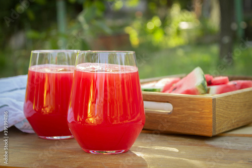 Two glasses with watermelon juice on a table in the garden. Wooden tray with watermelon slises photo