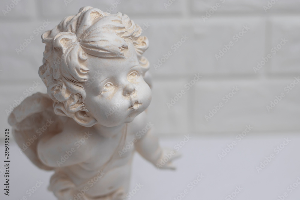 White plaster figurine of an angel on a brick wall background. Decorations in the interior.