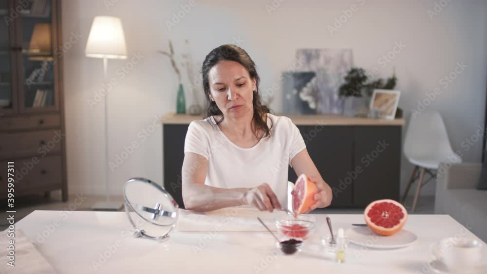 Medium shot of woman adding grapefruit pulp to bowl to make homemade scrub peeling for moistened and rejuvenated skin Medium shot of woman adding grapefruit pulp to bowl to make homemade scrub peeling for moistened and rejuvenated skin