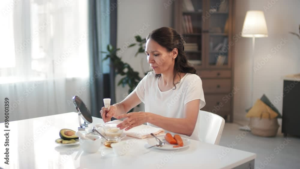 Medium shot of smiling attractive woman in mid 40s applying anti-aging mask made of carrot, avocado, egg and essential oils on face with brush Medium shot of smiling attractive woman in mid 40s applying anti-aging mask made of carrot, avocado, egg and essential oils on face with brush