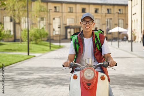 Young cheerful asian male courier with thermo bag delivering foo