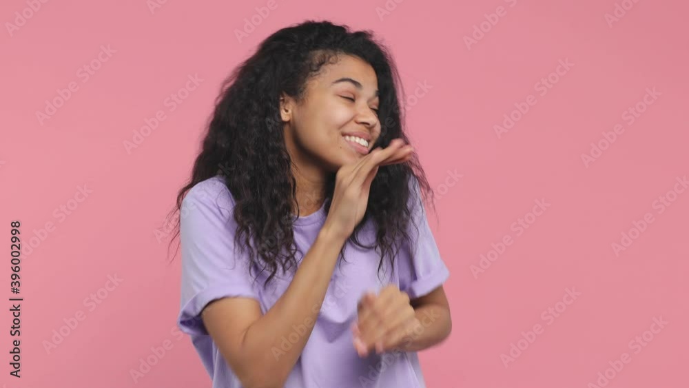 Cheerful funny young african american woman 20s years old in casual violet t-shirt posing isolated on pastel pink background in studio. People lifestyle concept. Dancing clenching fists waving hands Cheerful funny young african american woman 20s years old in casual violet t-shirt posing isolated on pastel pink background in studio. People lifestyle concept. Dancing clenching fists waving hands