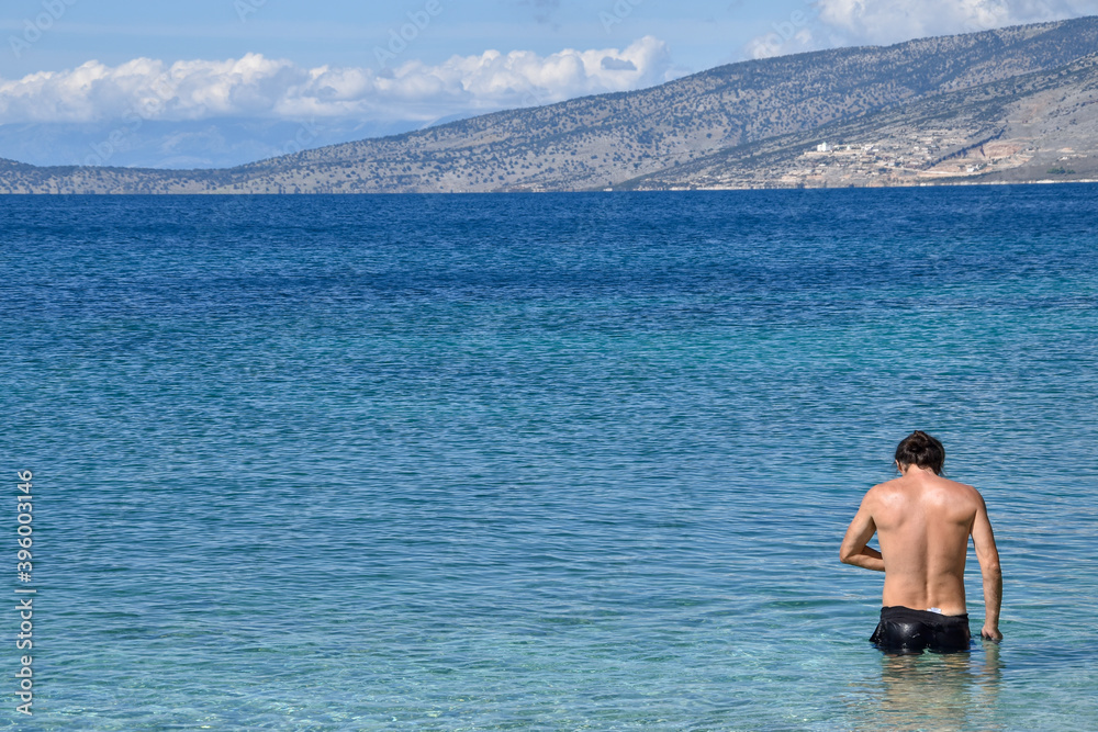 A handsome man enters the sea. A man goes swimming. Sunny day on the beach, blue sky above the blue sea.