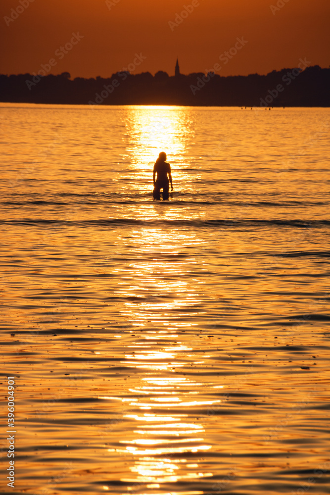 silhouette d'une jeune femme dans la mer devant un soleil couchant