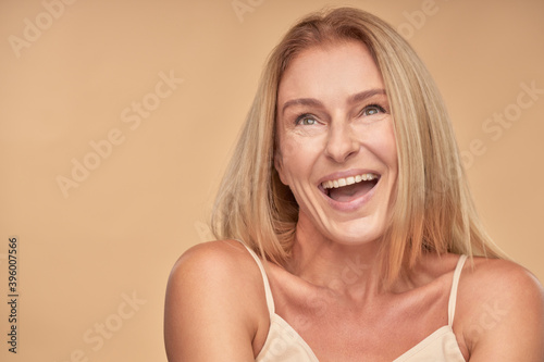 Pure happiness. Portrait of beautiful mature woman looking aside and laughing while posing in studio over beige background