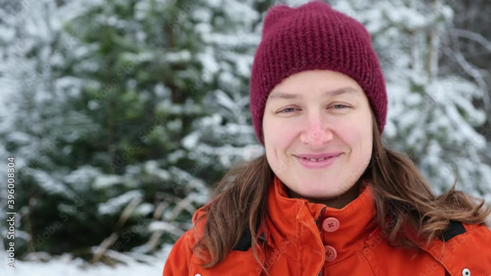 Winter portrait of cheerful smiling young woman without makeup in winter coat and knitted hat standing in snowy forest. Natural female beauty. Winter portrait of cheerful smiling young woman without makeup in winter coat and knitted hat standing in snowy forest. Natural female beauty.