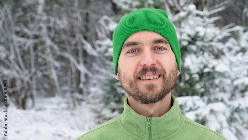 Portrait of handsome young bearded man in green knitted hat standing in snowy forest and looks at camera. Portrait of handsome young bearded man in green knitted hat standing in snowy forest and looks at camera.