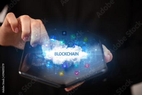 Businessman holding a foldable smartphone with BLOCKCHAIN inscription, technology concept