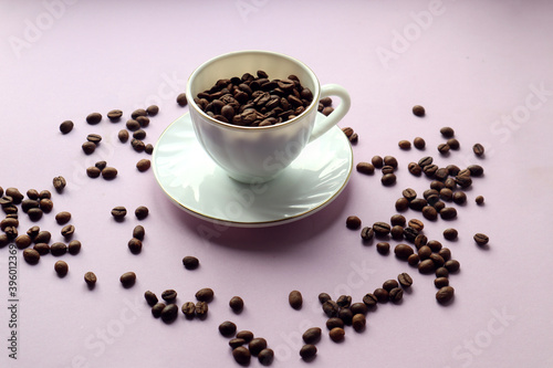 White Cup full of coffee beans on a pastel background and with scattered grains on it, side view - the concept of a pleasant coffee drinking