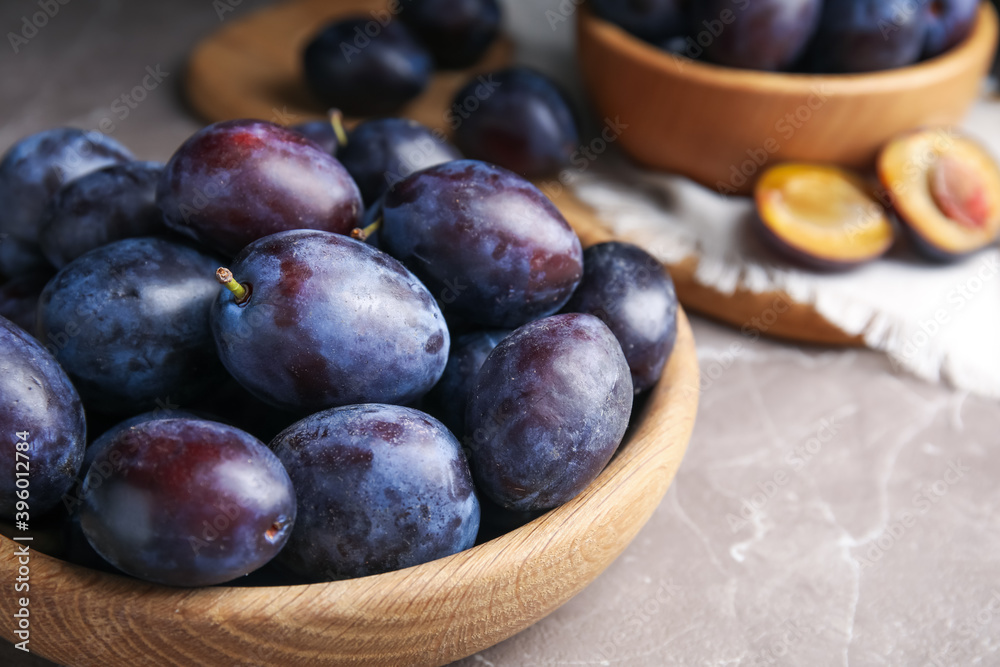 Delicious ripe plums in wooden bowl on grey marble table, closeup Delicious ripe plums in wooden bowl on grey marble table, closeup