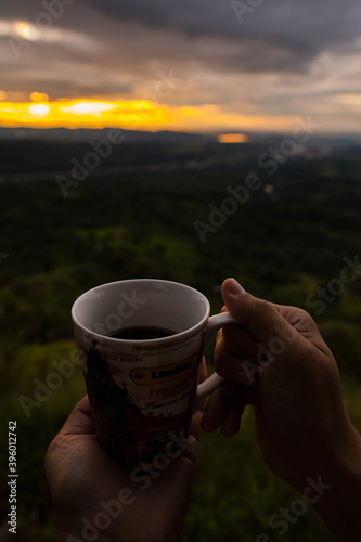 A person's hand holds a cup of coffee in the Colombian mountains.