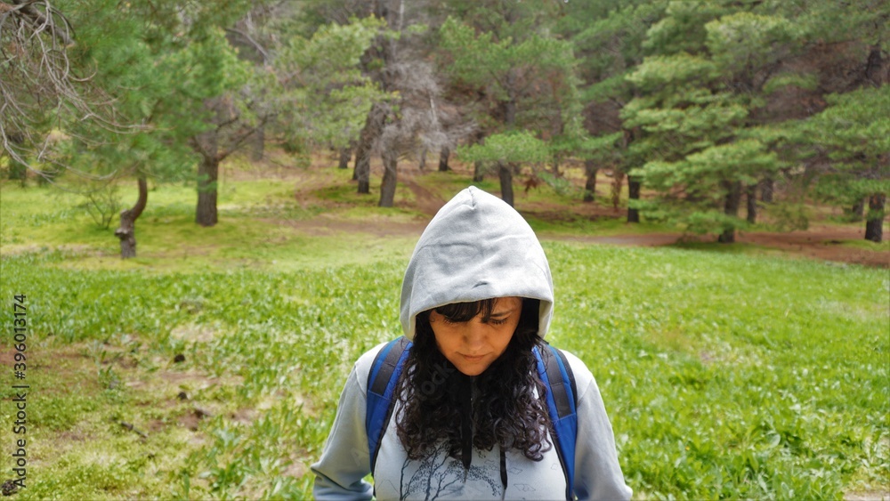 Middle aged woman with hood looking down in the middle of a pine forest