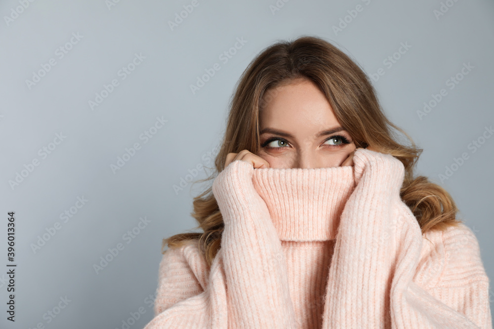 Happy young woman wearing warm sweater on grey background, space for text. Christmas celebration Happy young woman wearing warm sweater on grey background, space for text. Christmas celebration