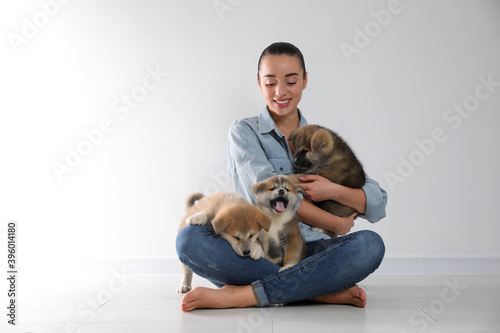 Woman with Akita Inu puppies sitting on floor near light wall