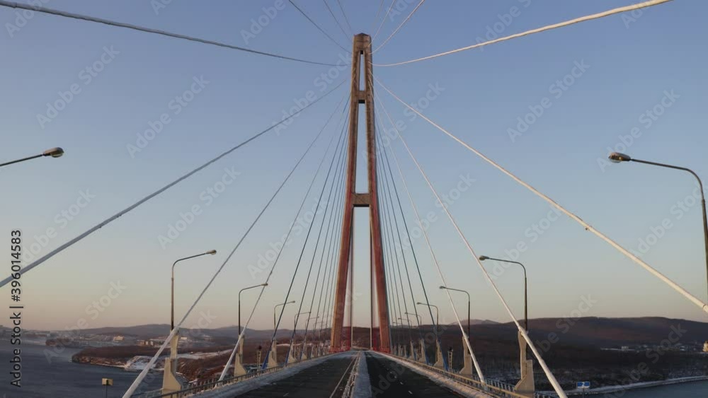 Flying above the empty road of the Russian Bridge. View from below of impressive high pillar against the blue sky. Morning. Vladivostok, Russia Flying above the empty road of the Russian Bridge. View from below of impressive high pillar against the blue sky. Morning. Vladivostok, Russia