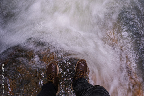 the boots of a person standing on the edge of a stream in the tropics.