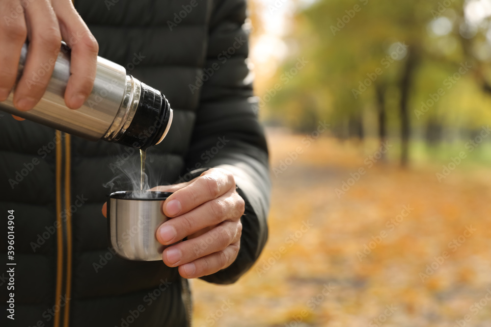 Fototapeta premium Man pouring drink from thermos into cap outdoors, closeup. Space for text
