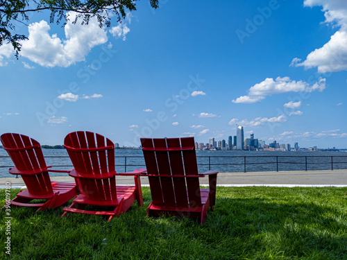 Three red lawn chairs with a view of Jersey City from Governors Island photo