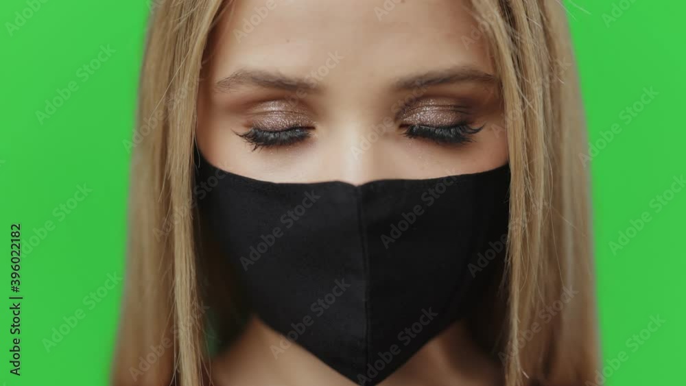 Close up of young woman with blond hair wearing black protective mask during quarantine time. Isolated over chroma key studio background. Infectious diseases. Close up of young woman with blond hair wearing black protective mask during quarantine time. Isolated over chroma key studio background. Infectious diseases.
