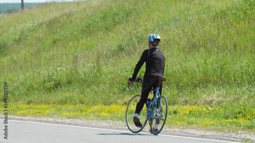 A professional cyclist in sports gear stopped at the side of the paved road to look back. A professional cyclist in sports gear stopped at the side of the paved road to look back.