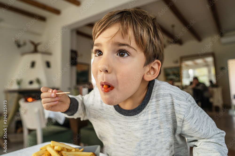 Portrait of small caucasian boy little child eating potato chips french fries at restaurant in sunny day while sitting by the table alone - healthy eating growing up concept Portrait of small caucasian boy little child eating potato chips french fries at restaurant in sunny day while sitting by the table alone - healthy eating growing up concept