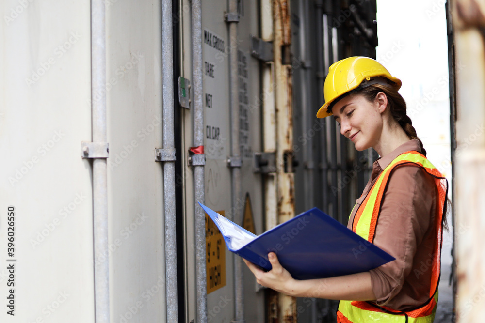 Young woman engineers standing in the shipping yard tracking the cargo inventory and checking container box for safety. Young woman engineers standing in the shipping yard tracking the cargo inventory and checking container box for safety.