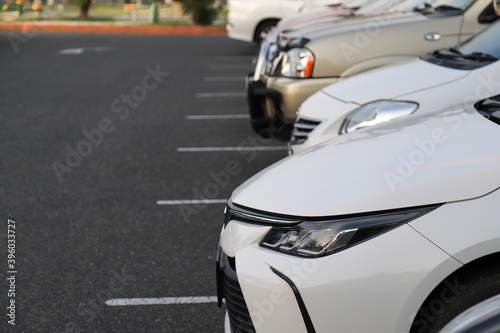 Closeup of front side of white car with other cars parking in outdoor parking area in the evening. 