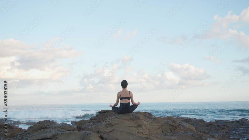 Beautiful panoramic view of a woman meditating on the seashore with waves crashing on the rocks Beautiful panoramic view of a woman meditating on the seashore with waves crashing on the rocks