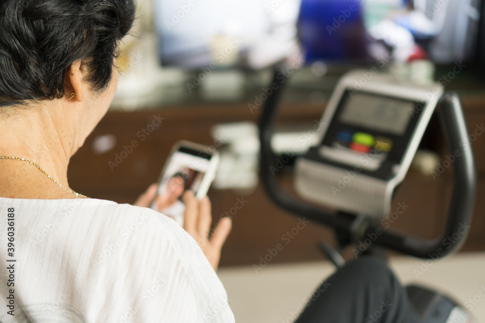 Φωτογραφία Active Asia senior old woman people training exercise on stationary bike for fit healthy  and  using smartphone to chat and  connect with aging society at home gym