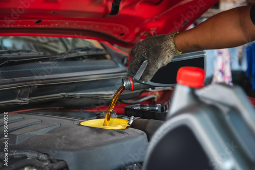 Car mechanic working in the local garage by pouring new oil into the engine. Oil change of car maintenance services.