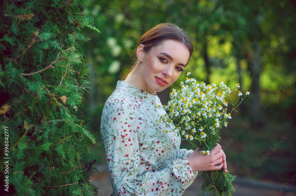 Beautiful young woman with a bouquet of field daisies on a walk