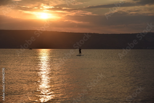 Man sail on a SUP board in a large lake during sunrise. Stand up paddle boarding - active recreation in nature. The Sea of Galilee, Lake Tiberias, Kinneret, Kinnereth. High quality photo.