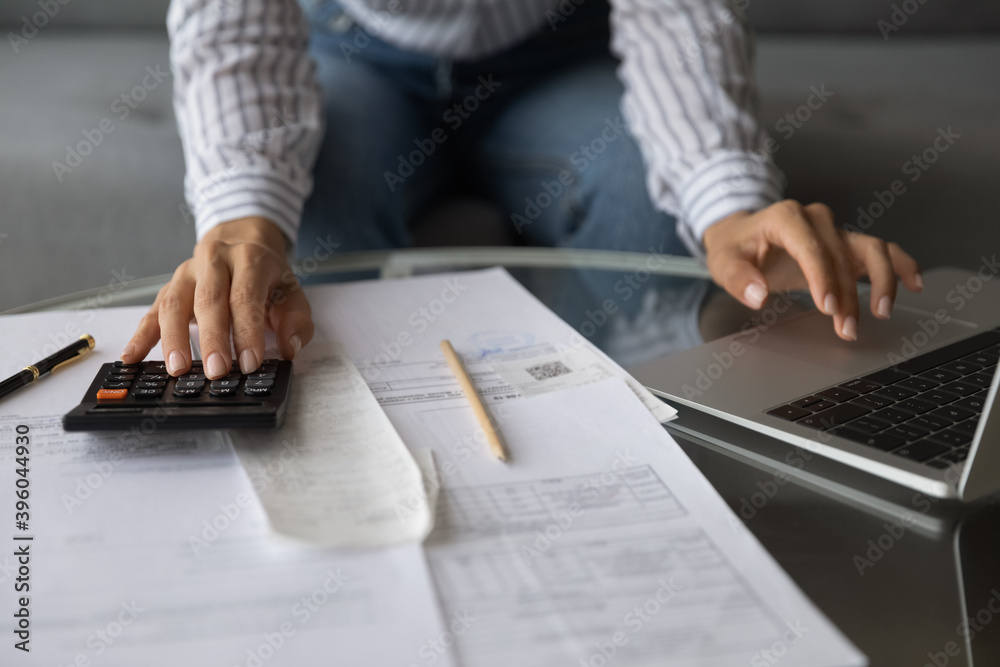 Fototapeta premium Crop close up of woman use calculator manage family financial budget pay bills online on computer. Female calculate count expenses expenditures, work with paperwork at home. Saving, finances concept.