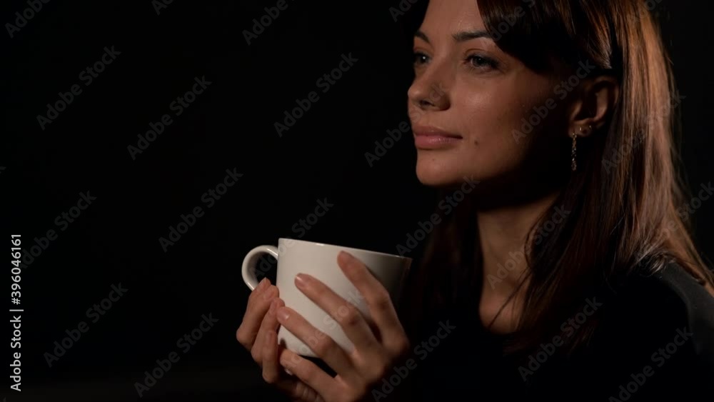 sexual and seductive young woman is smiling sitting in black background, holding tea cup in hands sexual and seductive young woman is smiling sitting in black background, holding tea cup in hands