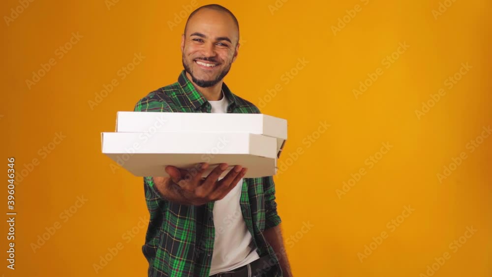 African american man in green shirt gives you two boxes of pizza dekivery against yellow abckground African american man in green shirt gives you two boxes of pizza dekivery against yellow abckground