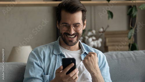 Wide banner panoramic view of excited young Caucasian man look at smartphone screen celebrate online win or victory. Happy millennial male triumph feel excited with good news on cellphone gadget.