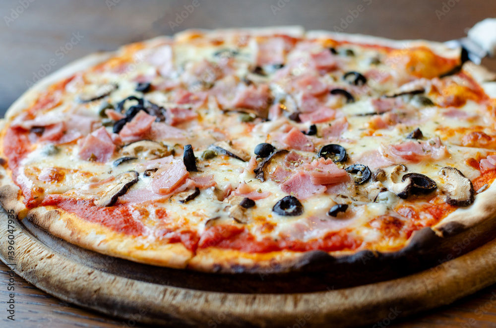 Delicious homemade ham pizza served on wooden plate, selective focus