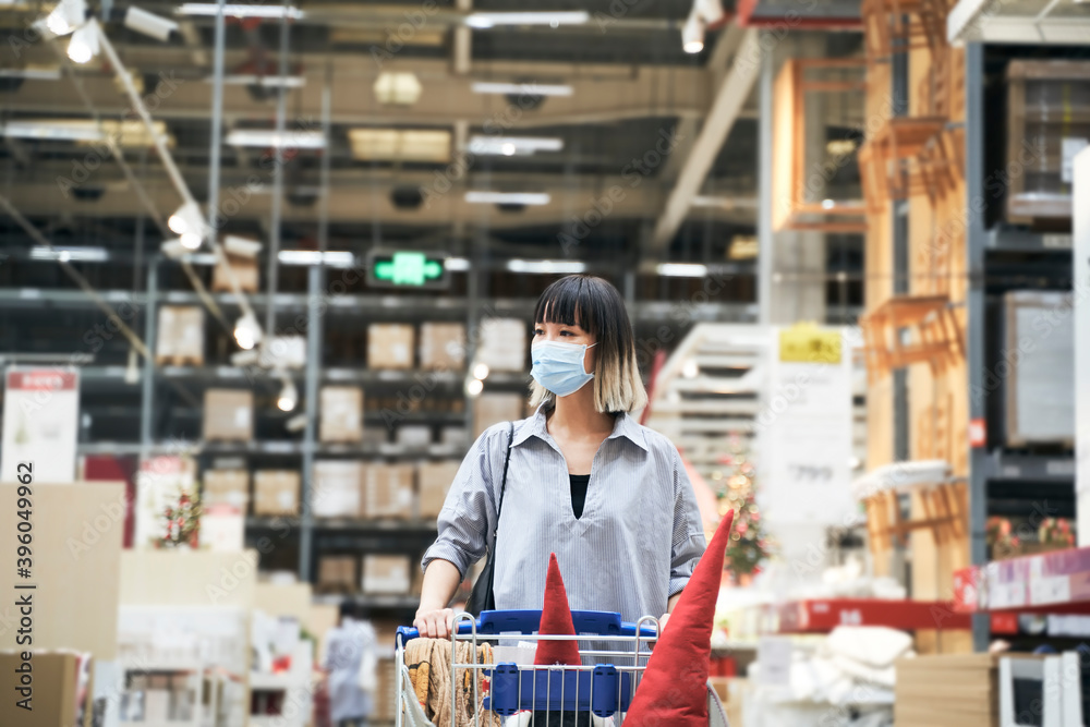 Asian woman wearing face mask push shopping cart in warehouse store buying Christmas decorations & gifts