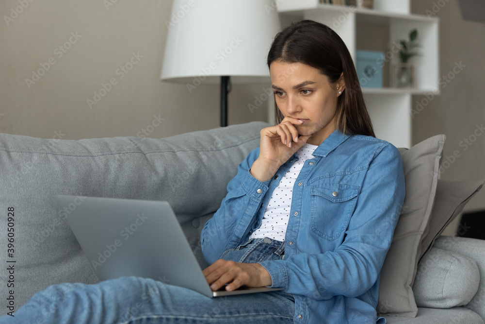 Pensive millennial Caucasian woman sit on sofa at home look at laptop screen thinking pondering working online. Thoughtful millennial female use computer consider problems solution or option. Pensive millennial Caucasian woman sit on sofa at home look at laptop screen thinking pondering working online. Thoughtful millennial female use computer consider problems solution or option.