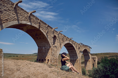 woman traveler Explorer in a black hat sit next to the destroyed old stone bridge in the summer photo