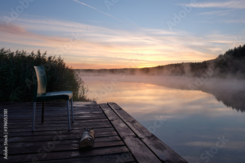 Fototapeta Naklejka Na Ścianę i Meble -  Summer, lake, early morning, beautiful sky, fog over the water. A wooden dock with an empty chair.