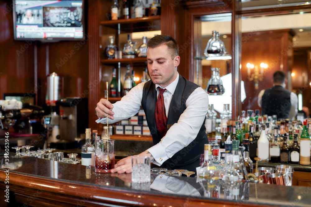 Less thinking more drinking. Young bartender standing at counter and mixing alcohol while making iced cocktail in the bar