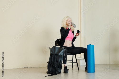 Pretty fit young woman in sports clothes drinking water after training in health club photo