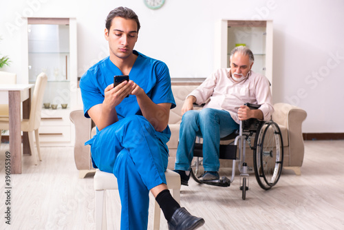 Old man in wheel-chair and young bad caregiver indoors